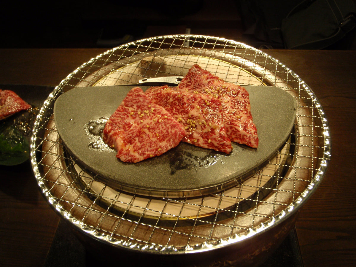黒玄武プレートの上で焼ける牛肉(店内・暗い卓)